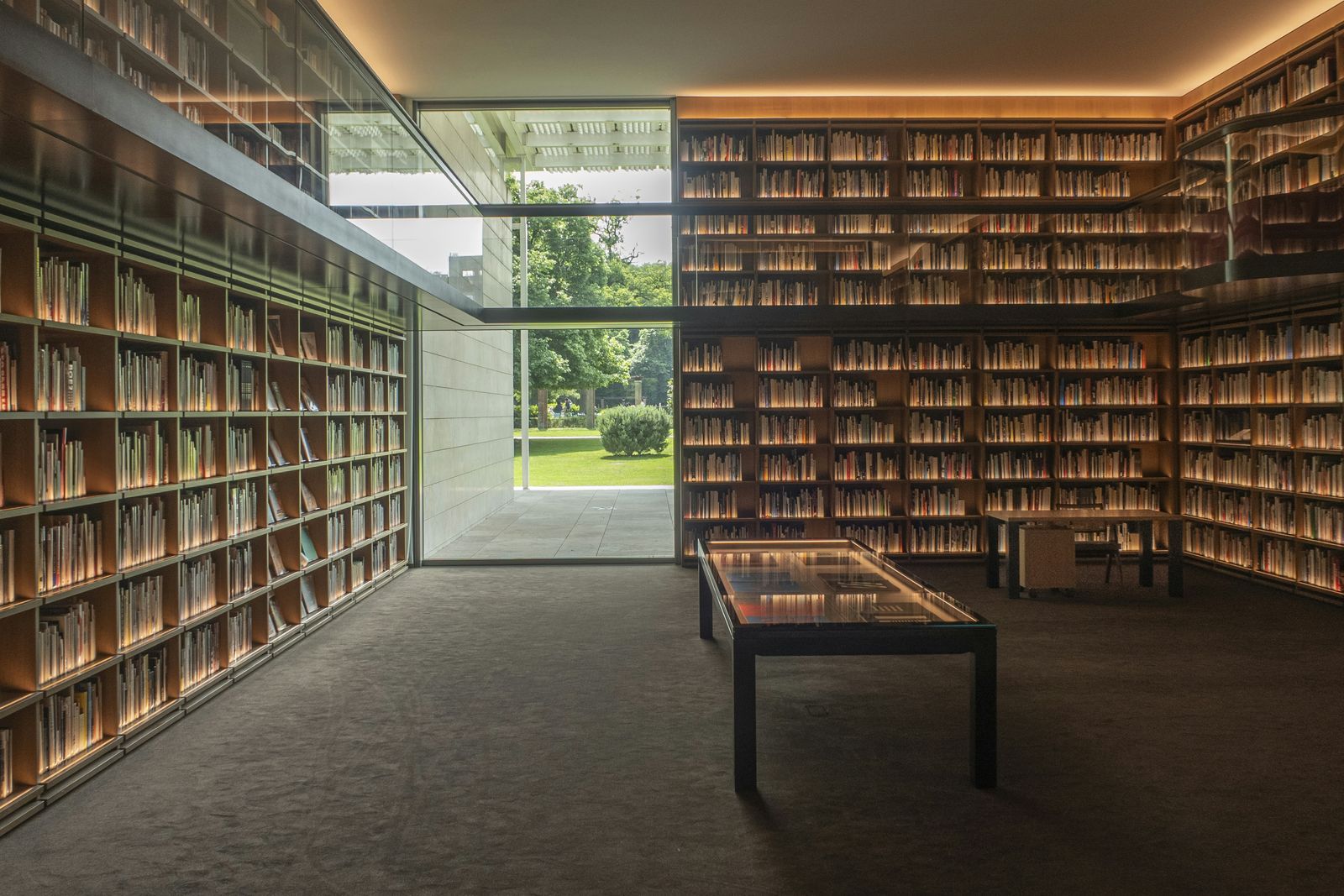 Modern library with floor-to-ceiling bookshelves around a glass-walled reading room